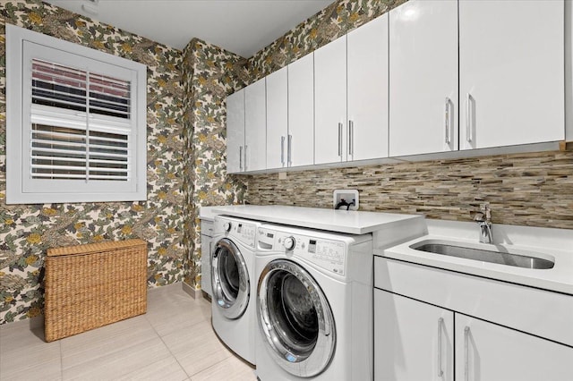 laundry room with cabinet space, wallpapered walls, separate washer and dryer, and a sink