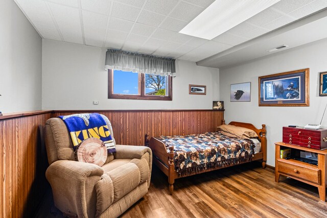 bedroom featuring visible vents, wood finished floors, wainscoting, and wood walls