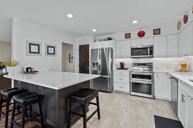 kitchen with tasteful backsplash, a breakfast bar, appliances with stainless steel finishes, white cabinets, and a peninsula