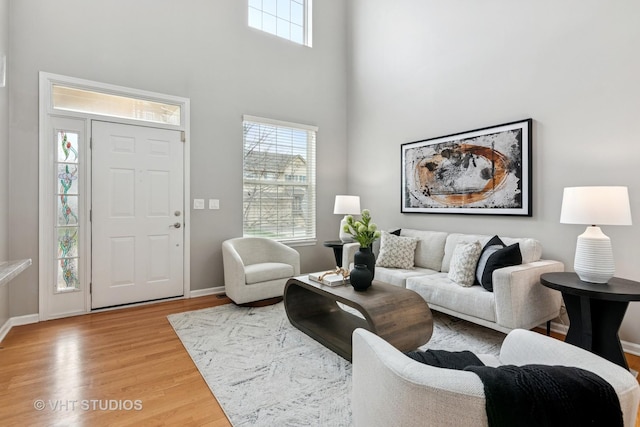 living area with light wood-type flooring, baseboards, and a high ceiling