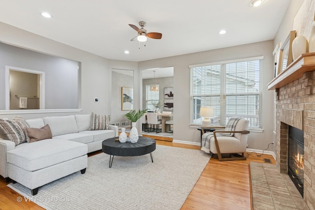 living area with a ceiling fan, a brick fireplace, recessed lighting, and light wood-style floors
