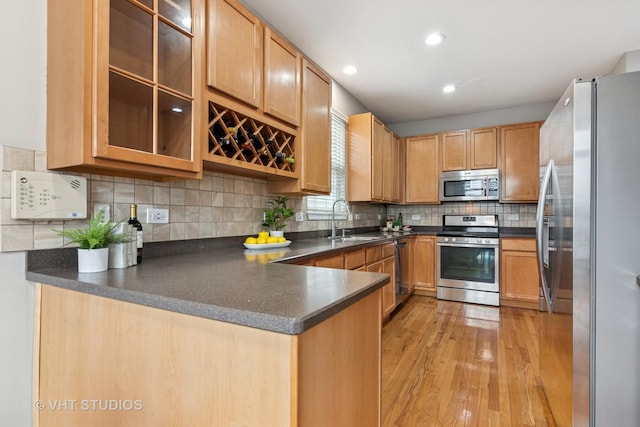 kitchen featuring dark countertops, a sink, light wood finished floors, a peninsula, and appliances with stainless steel finishes