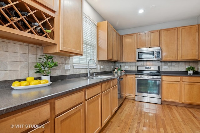 kitchen with a sink, dark countertops, backsplash, light wood-style floors, and appliances with stainless steel finishes