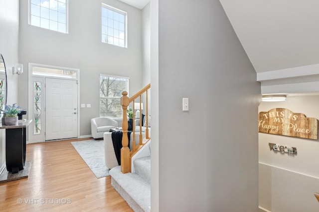 entryway with baseboards, light wood-style flooring, a high ceiling, and stairs