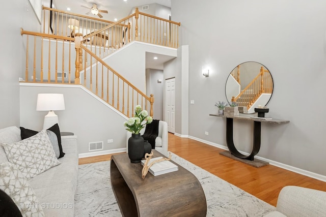 living room with wood finished floors, visible vents, stairs, and ceiling fan