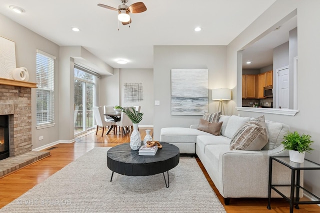 living area with recessed lighting, light wood-style floors, a brick fireplace, and baseboards