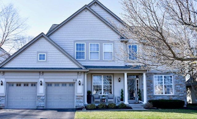 craftsman house featuring driveway, stone siding, a front lawn, and covered porch