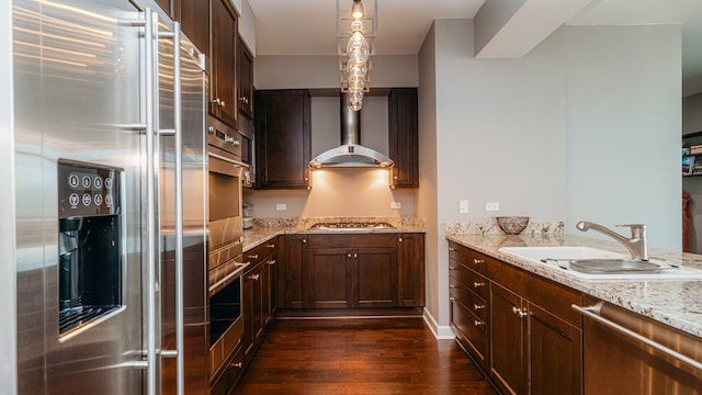 kitchen featuring stainless steel appliances, wall chimney exhaust hood, dark wood finished floors, a sink, and light stone countertops