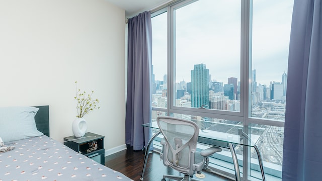 bedroom with wood finished floors, baseboards, a view of skyline, an office area, and floor to ceiling windows