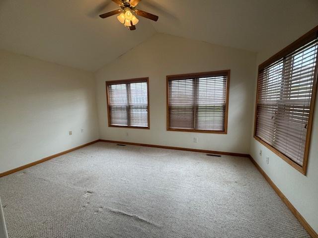 spare room featuring lofted ceiling, light carpet, baseboards, and ceiling fan
