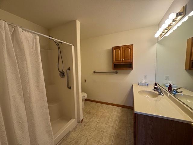 bathroom featuring toilet, a shower with curtain, vanity, and baseboards