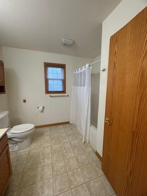 bathroom featuring toilet, vanity, shower / bathtub combination with curtain, baseboards, and visible vents