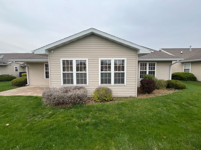 rear view of property with a patio area, roof with shingles, and a yard