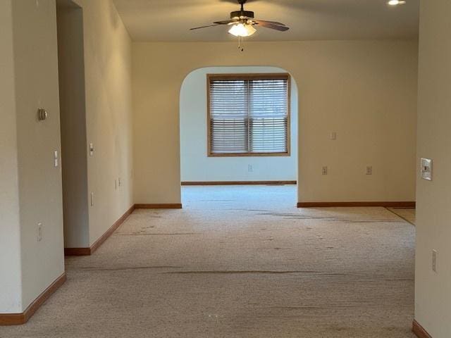 empty room with carpet, baseboards, arched walkways, and ceiling fan
