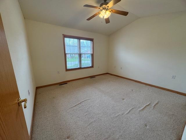 carpeted spare room featuring vaulted ceiling, visible vents, baseboards, and ceiling fan