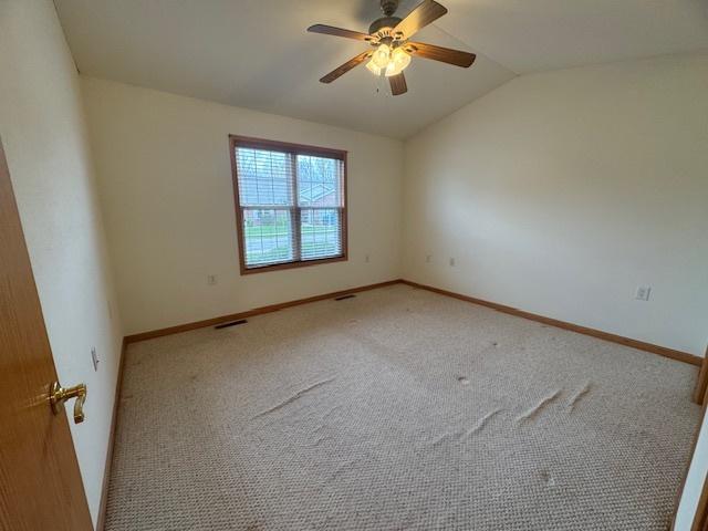 carpeted empty room featuring ceiling fan, lofted ceiling, visible vents, and baseboards