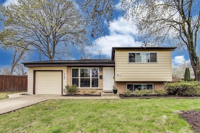 split level home featuring concrete driveway, a front yard, an attached garage, and fence