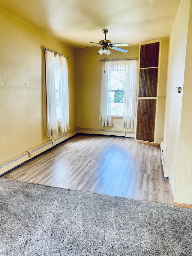 empty room with a baseboard heating unit, ceiling fan, wood finished floors, and a healthy amount of sunlight