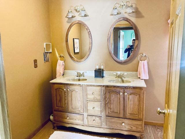 full bath featuring double vanity, wood finished floors, baseboards, and a sink