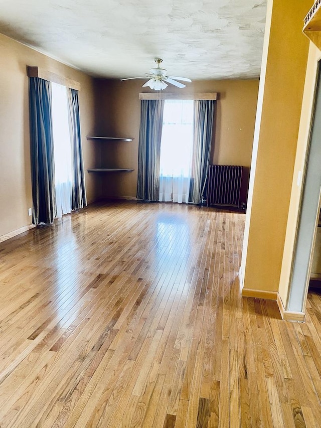 spare room with ceiling fan, baseboards, light wood finished floors, radiator heating unit, and built in features