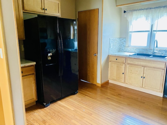 kitchen with light wood-style flooring, decorative backsplash, light countertops, a sink, and black fridge
