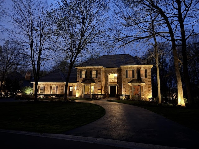 colonial inspired home featuring brick siding, curved driveway, stone siding, and a front lawn