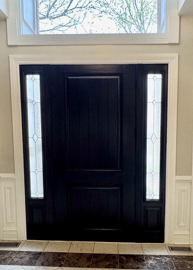 entrance foyer featuring visible vents, a decorative wall, and a wainscoted wall