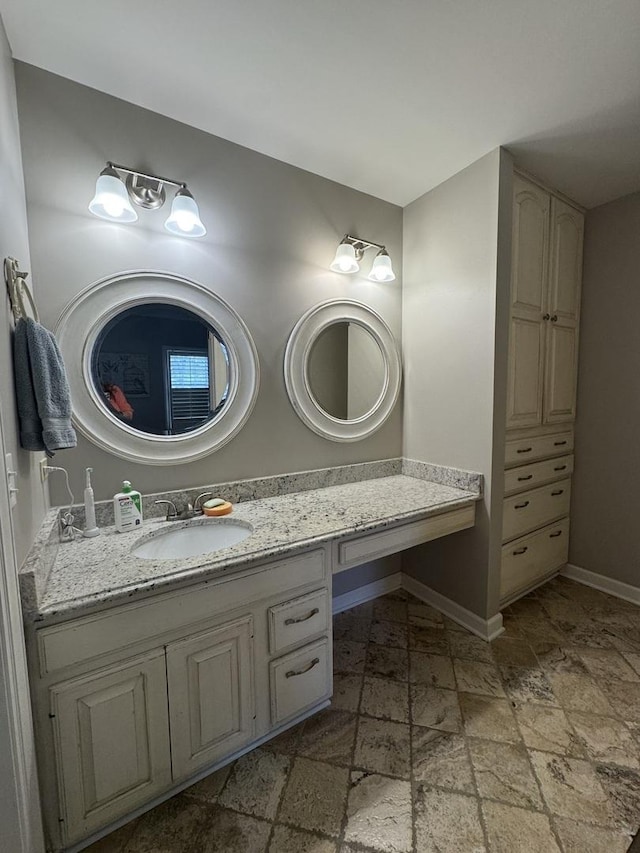 bathroom with stone tile flooring, baseboards, and vanity