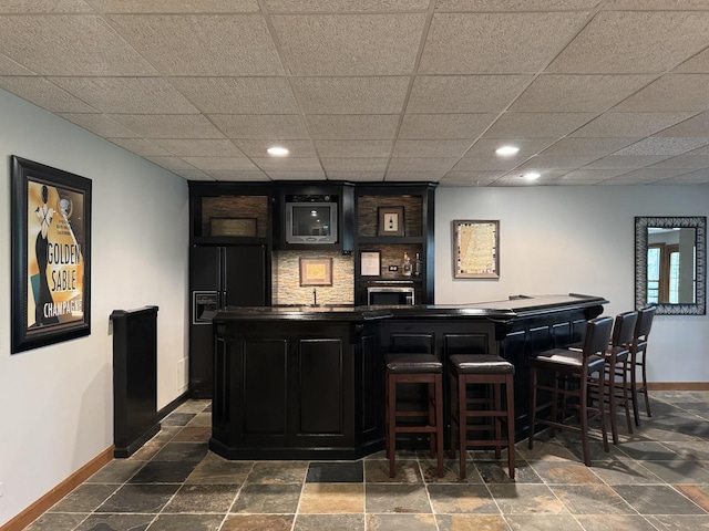 bar featuring stone finish floor, wet bar, black fridge with ice dispenser, baseboards, and recessed lighting