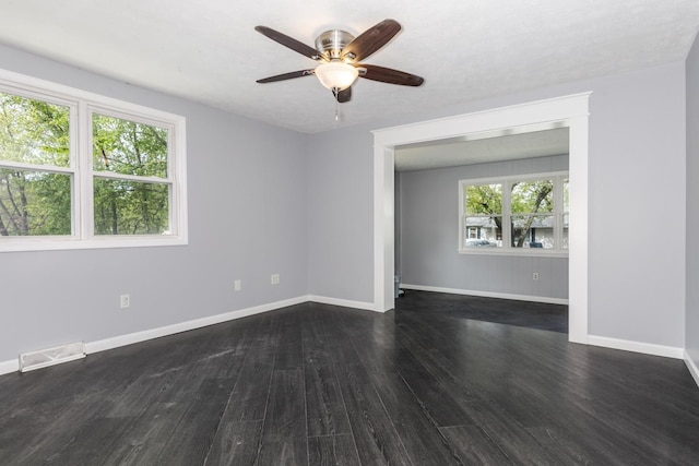 empty room with baseboards, a ceiling fan, dark wood finished floors, and visible vents