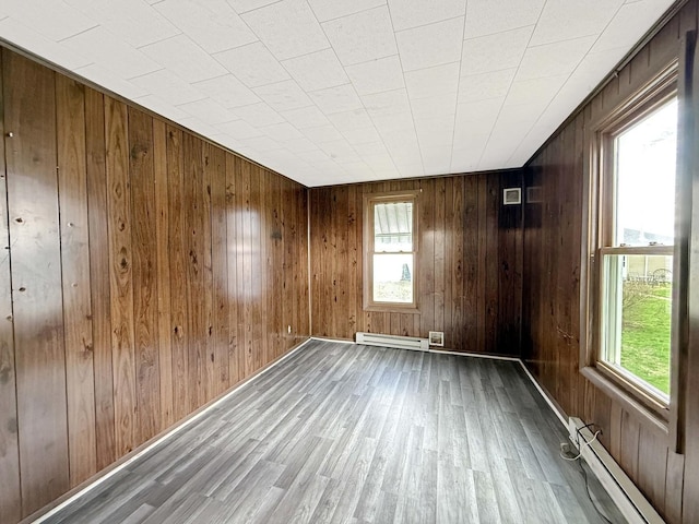 empty room with a baseboard heating unit, wood finished floors, a wealth of natural light, and a baseboard radiator