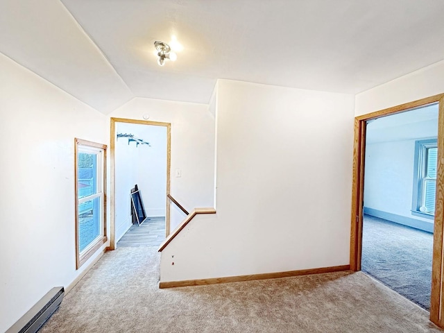 corridor featuring vaulted ceiling, baseboards, baseboard heating, and light colored carpet