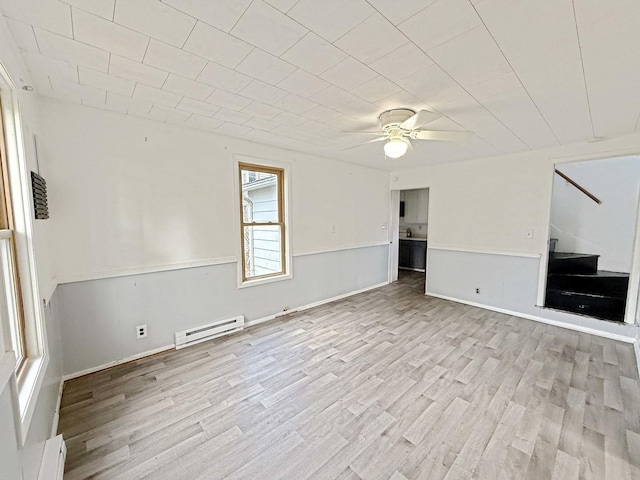 empty room featuring a baseboard radiator, wood finished floors, stairs, and ceiling fan