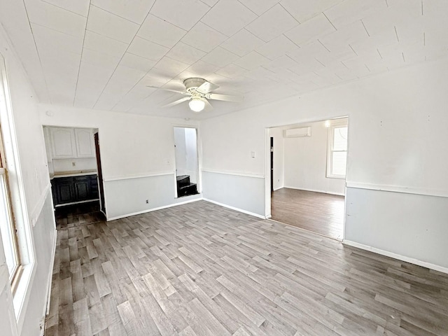 unfurnished living room with a wall mounted air conditioner, ceiling fan, and wood finished floors