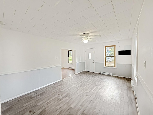 empty room featuring wood finished floors, baseboard heating, ceiling fan, and wainscoting