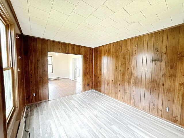 empty room with a baseboard heating unit, a baseboard radiator, wood finished floors, and wooden walls