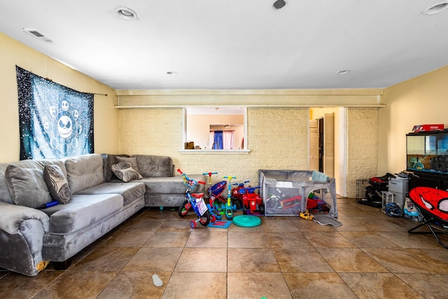 living room featuring stone finish flooring, brick wall, and visible vents
