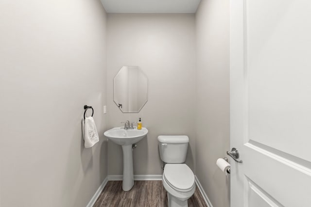 half bathroom featuring baseboards, wood finished floors, a sink, and toilet