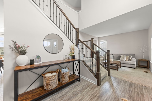 stairs featuring wood finished floors, a high ceiling, baseboards, and plenty of natural light