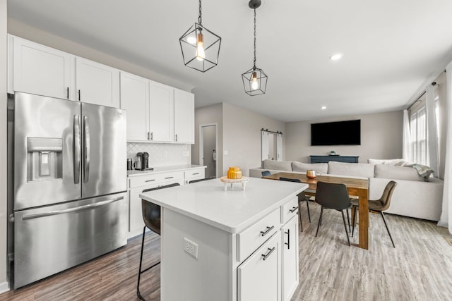 kitchen featuring open floor plan, light wood-style floors, stainless steel fridge with ice dispenser, light countertops, and a kitchen island