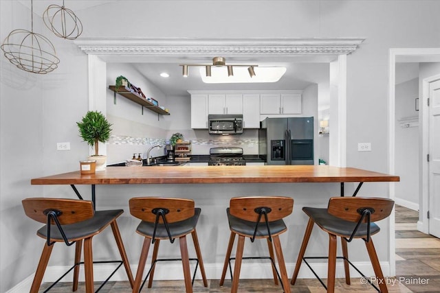 kitchen featuring butcher block countertops, a kitchen bar, backsplash, a peninsula, and appliances with stainless steel finishes