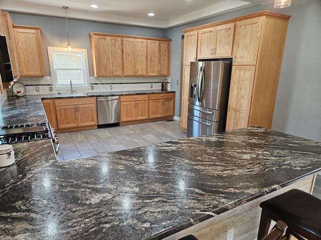 kitchen featuring appliances with stainless steel finishes, tasteful backsplash, a sink, recessed lighting, and dark stone countertops