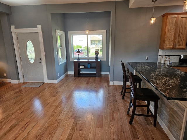 kitchen featuring light wood-type flooring, baseboards, brown cabinets, pendant lighting, and dark stone counters