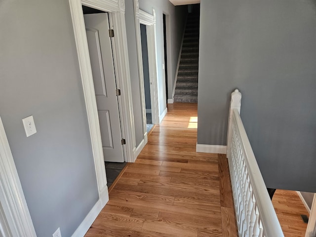 corridor with an upstairs landing, baseboards, and light wood-style floors