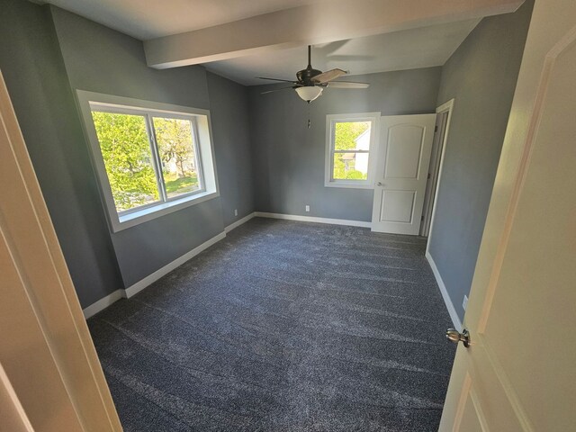 unfurnished room with plenty of natural light, dark carpet, baseboards, a ceiling fan, and beam ceiling