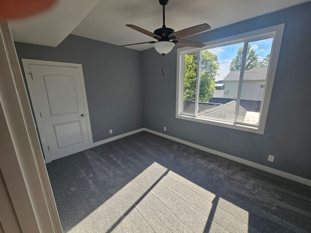 unfurnished room featuring dark carpet, a ceiling fan, and baseboards