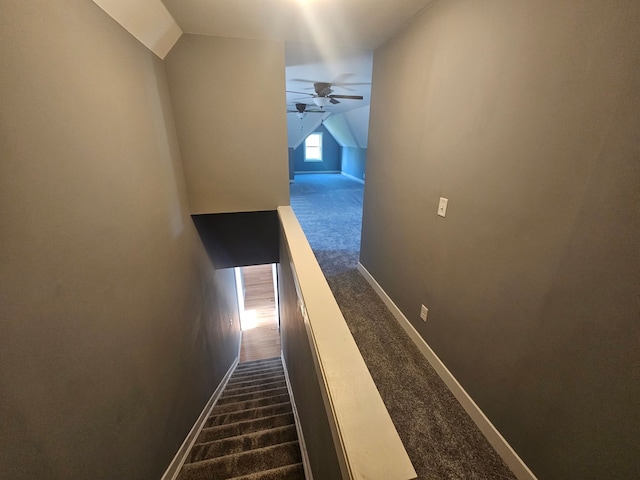 corridor featuring dark carpet, lofted ceiling, and baseboards