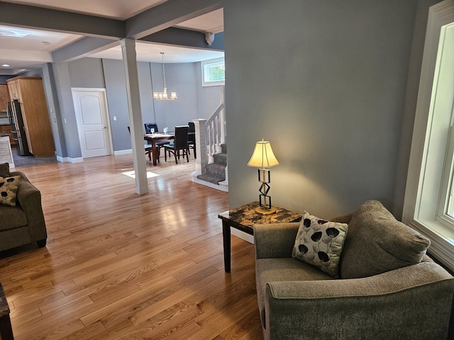 living room featuring a chandelier, stairs, light wood-style floors, baseboards, and beam ceiling