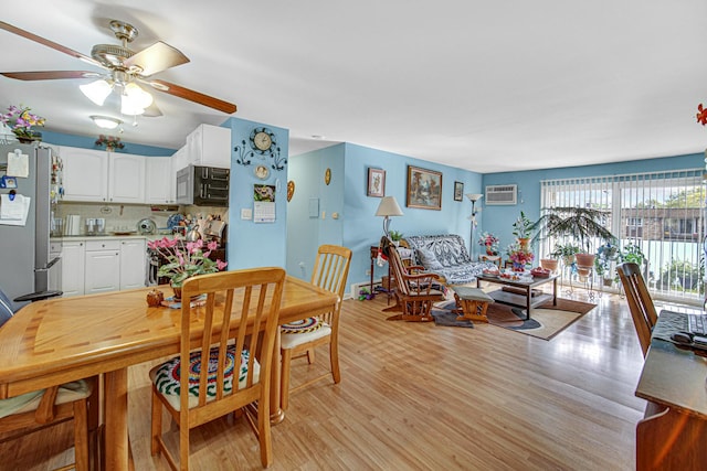 dining area featuring ceiling fan, a wall unit AC, and light wood-style flooring