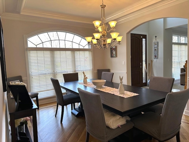 dining area featuring arched walkways, an inviting chandelier, ornamental molding, and wood finished floors